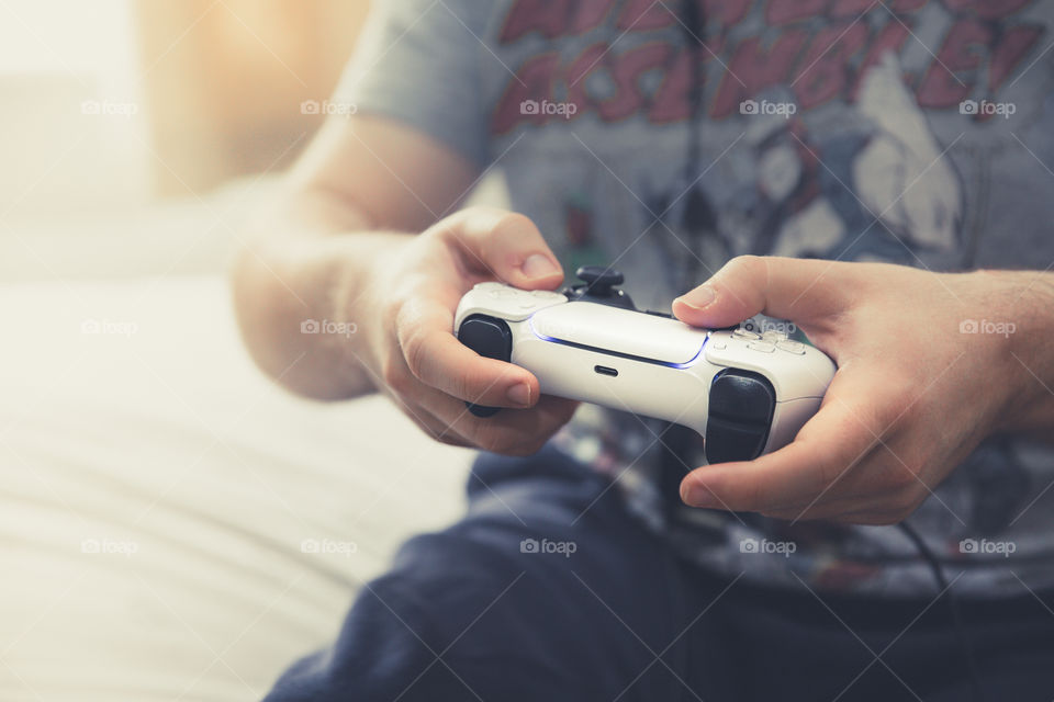A teenage gamer holding a video games remote controller and playing video games in his bedroom with copy space