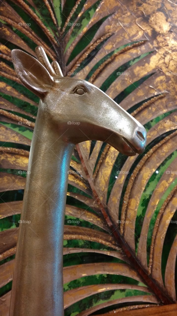 Metal giraffe. A tall, metallic giraffe, in front of a tall, metallic plant...