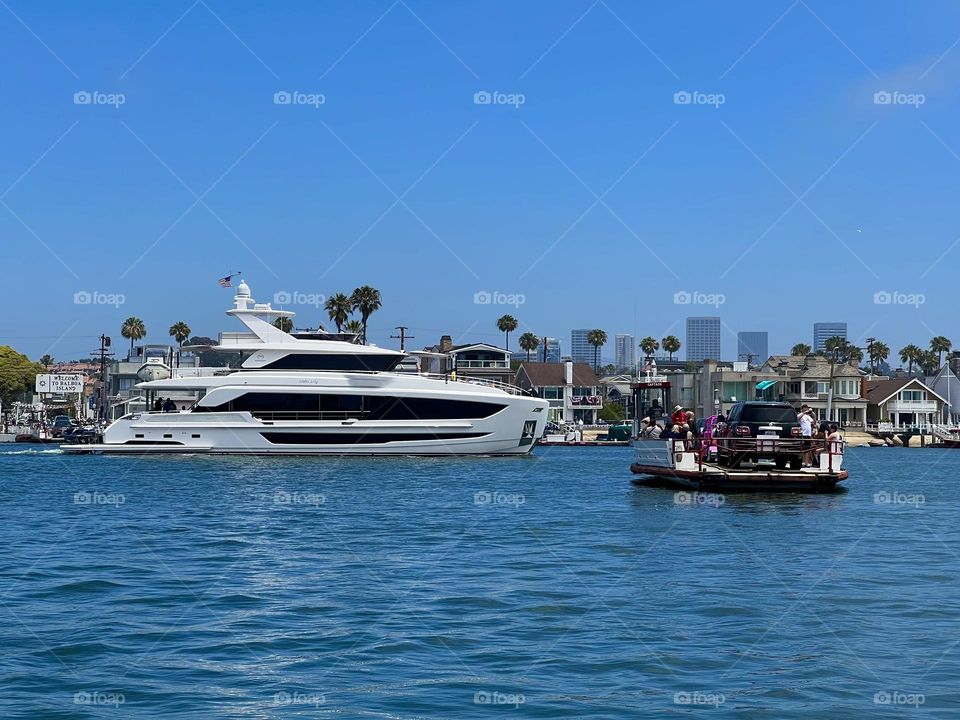 Balboa Island Ferry crossing the Entrance Channel in Newport Beach California with a yacht in front of it 