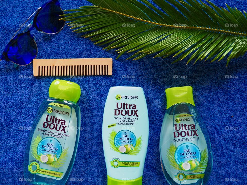 Garnier shampoo, conditioner and bath gel on a blue towel with comb, sunglasses and palm leaf.