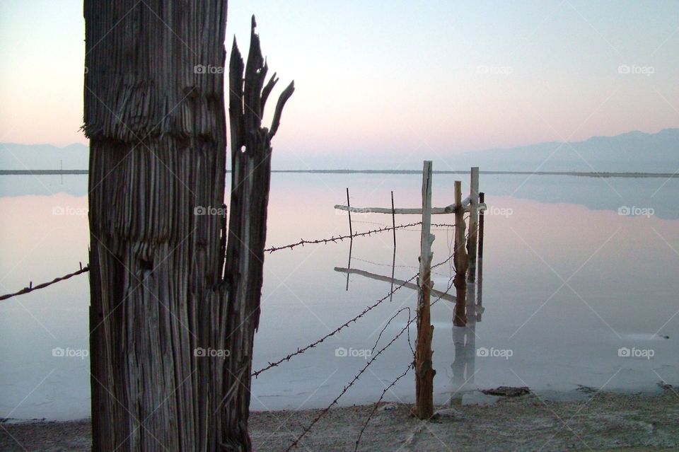 Fence post and barbed wire trailing off into the Great Salt Lake in the morning light of the early dawn