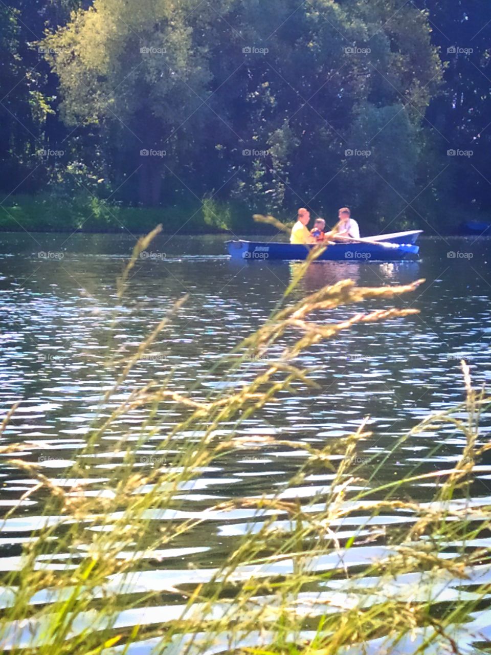The family is sailing in a wooden boat on a summer day.  Around the forest