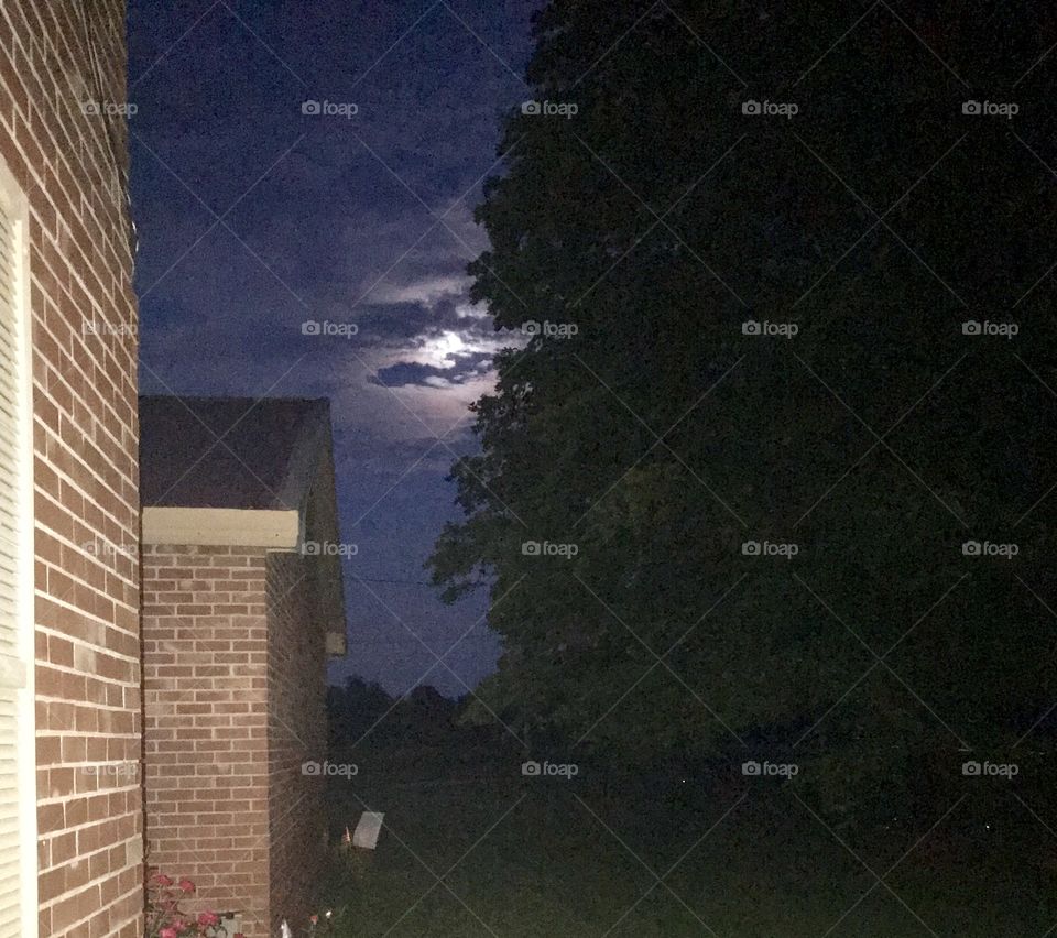 Beautiful view from the front porch of a full moon peeking out from behind the clouds. 