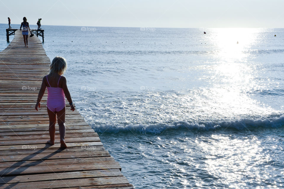 Little girl walking on a bridge at the beach looking down in the water. The girl i four years old and this is Alcudia Majorca.