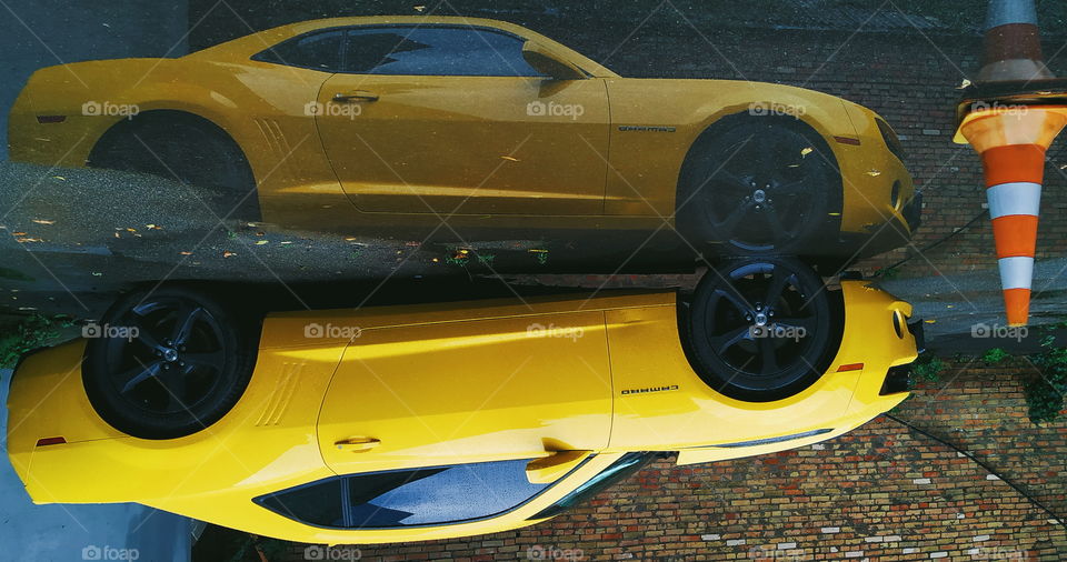 reflection of a yellow chevrolet car in a rain puddle