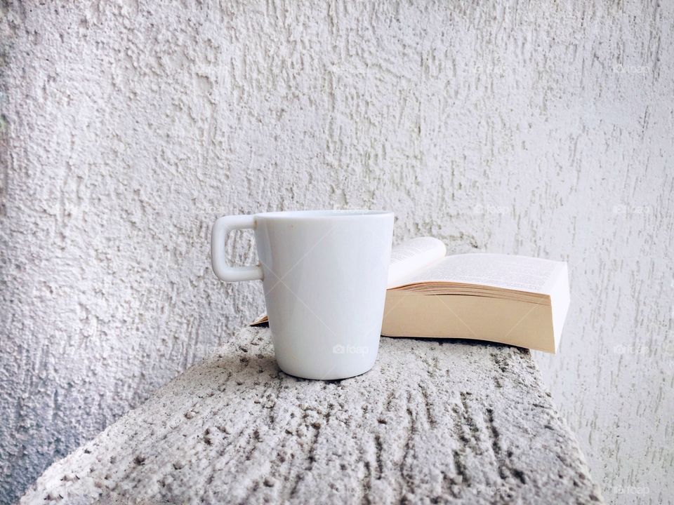 White cup of coffee and book with a white minimalistic background 
