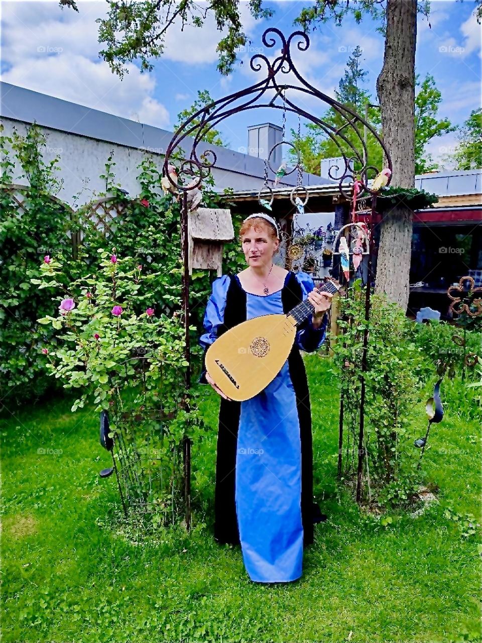 This lady has a love for music and tradition. She wears a medieval to Renaissance inspired gown and plays a lute custom built after a historical model in her beautiful garden in „Lower Bavaria“, Germany. 2024. Hypnotic Productions