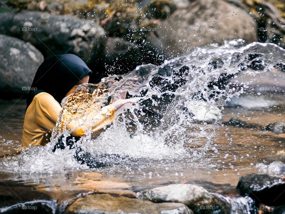 A woman in hijab playing with water splash in a rainforest stream