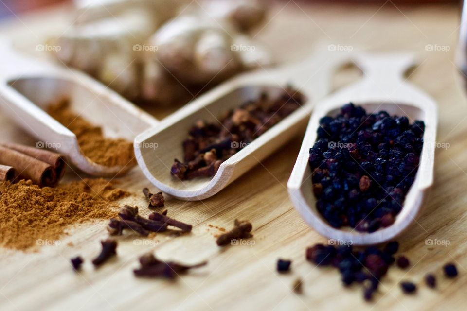 Closeup of ground cinnamon and cinnamon sticks, ginger root, whole cloves, and dried elderberries in wooden scoops on a wooden surface as ingredients for homemade syrup 