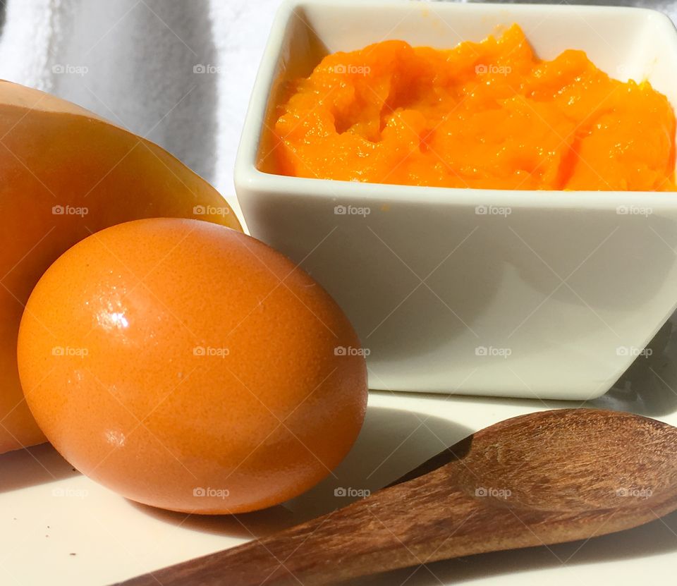 Orange mashed squash in white dish with orange brown egg foreground 