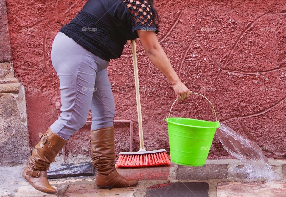 A women is pouring a bucket of soapy water on the sidewalk in San Miguel de Allende, Mexico