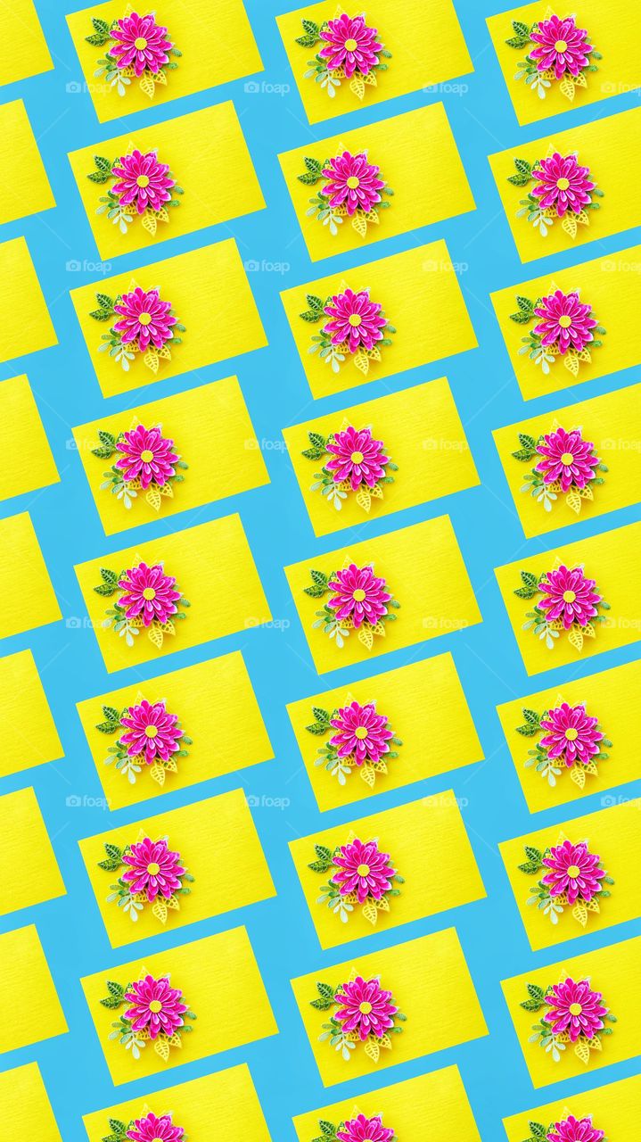 the pattern of a pink bright flower with leaves on a yellow sheet of paper is repeated on a blue background.