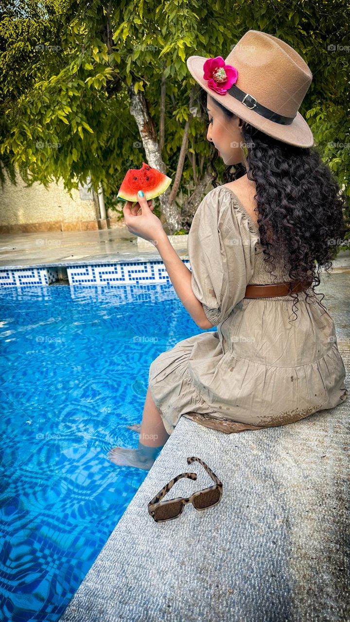 Curly-haired girl holding a watermelon by the pool