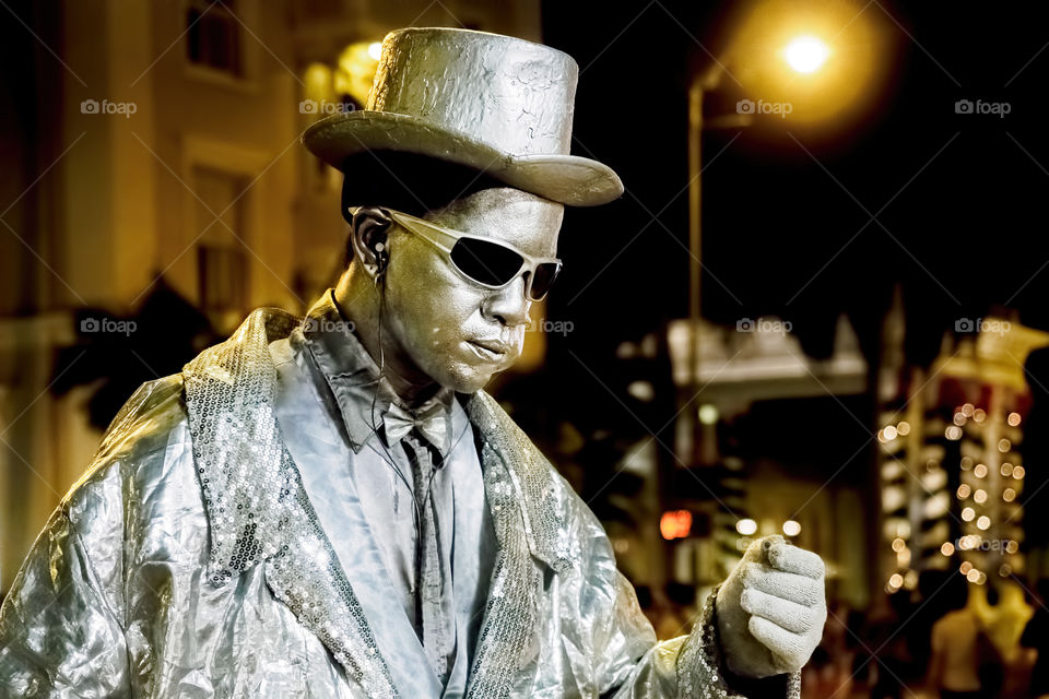 Waikiki, Honolulu, Hawaii, USA - December 12, 2015: Night street performer along Kalakaua Avenue keeping very still and does not move. His face is painted glittery silver match his clothing color. Passers-by watch in amazement and often donate money.