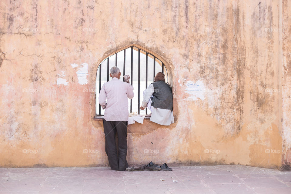 Two men in India look outside, through a window in a fort.