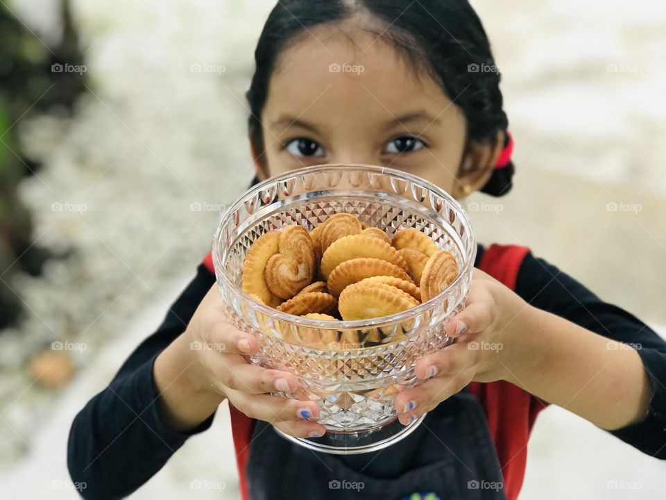 Baby girl holding a designed glass bowl full of cookies and showing towards the camera and smiling ☺️