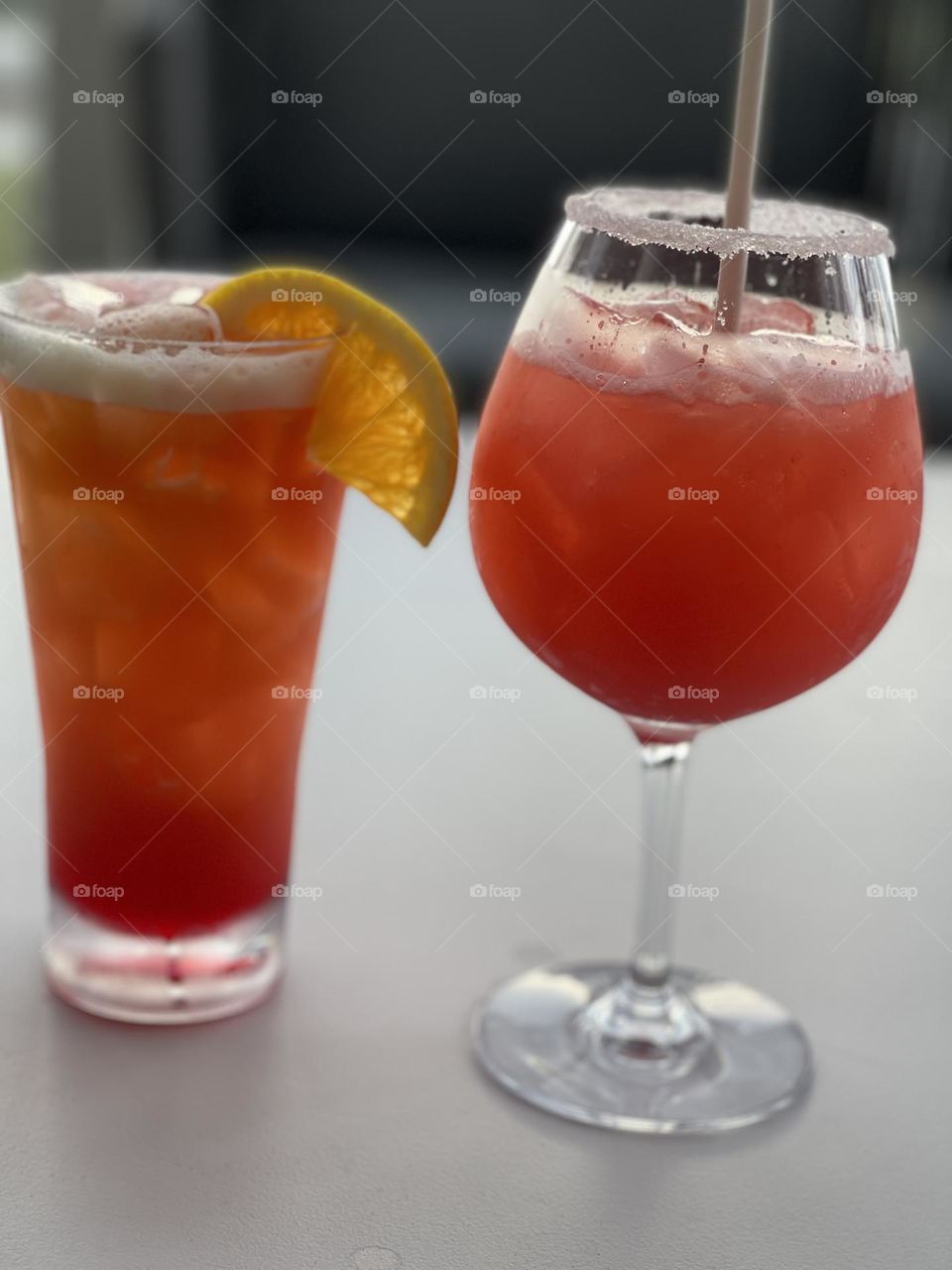 Two cocktails are ready to be sipped. The drinks are garnished with a lemon and salt. The beautifully colored drinks shine in the daylight.