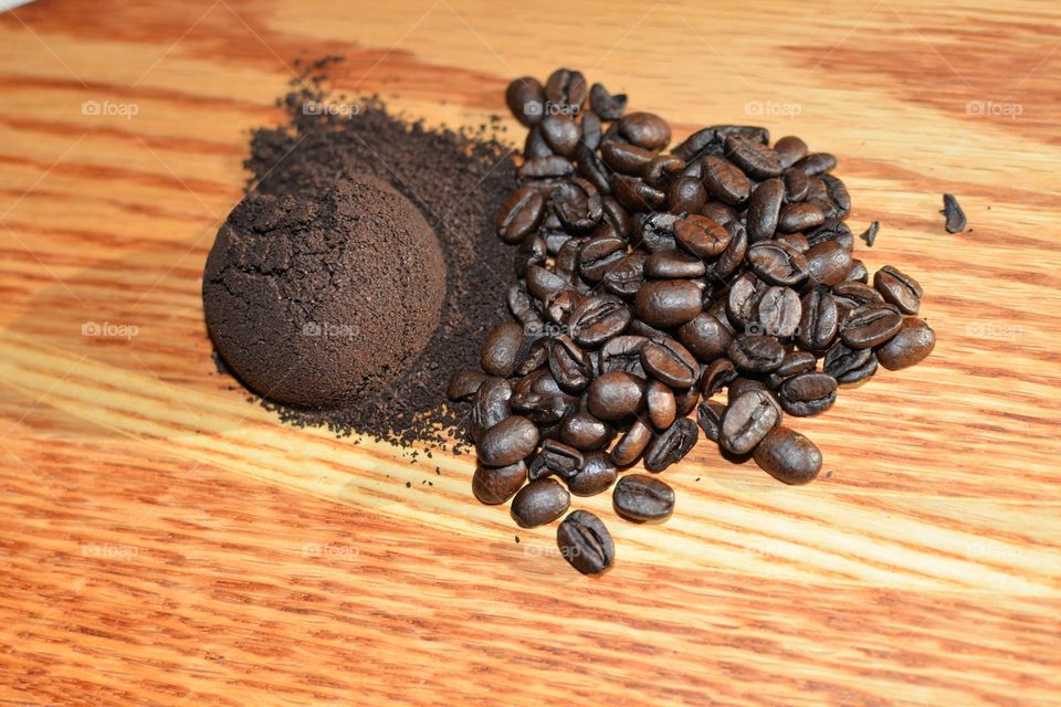 Coffee beans and a rounded scoop of ground coffee beans on an orange-colored wood cutting board 