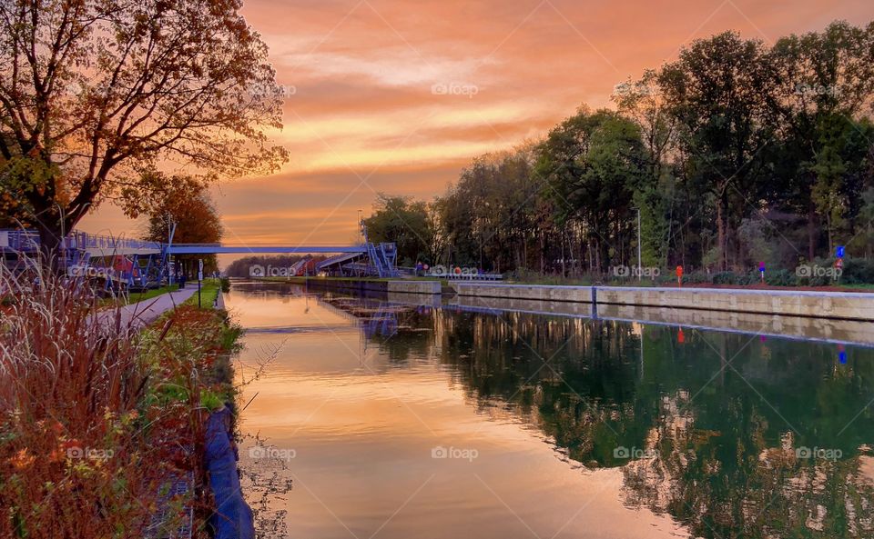 Orange colored sunrise sky reflected in the water of a river in a fall Countryside landscape 