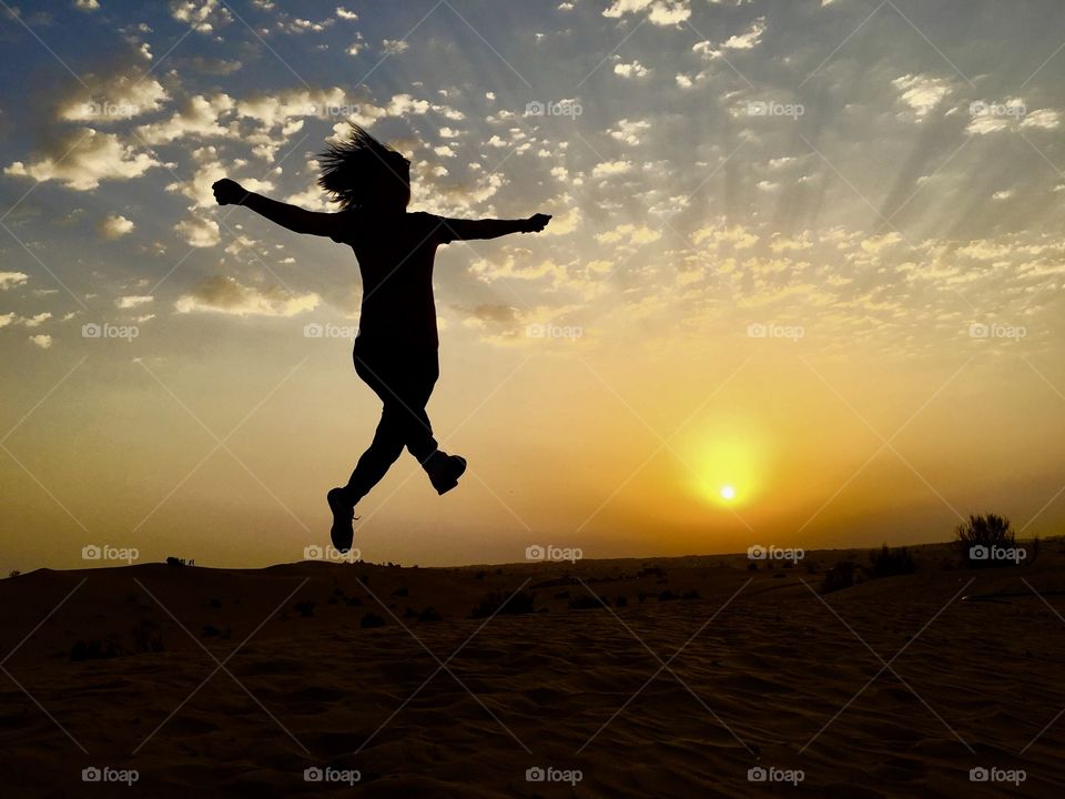 Silhouette of a woman jumping in the desert during sunset 