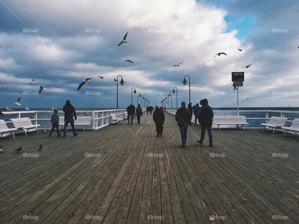 People walking on jetty at calm sea