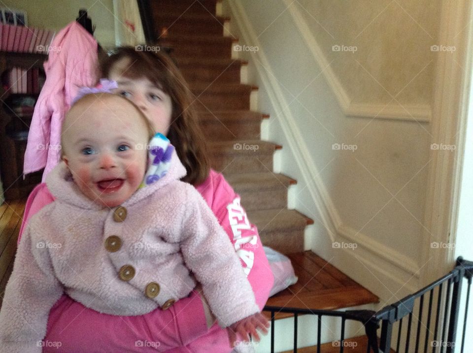 Baby with Down syndrome being held by her sister, smiling