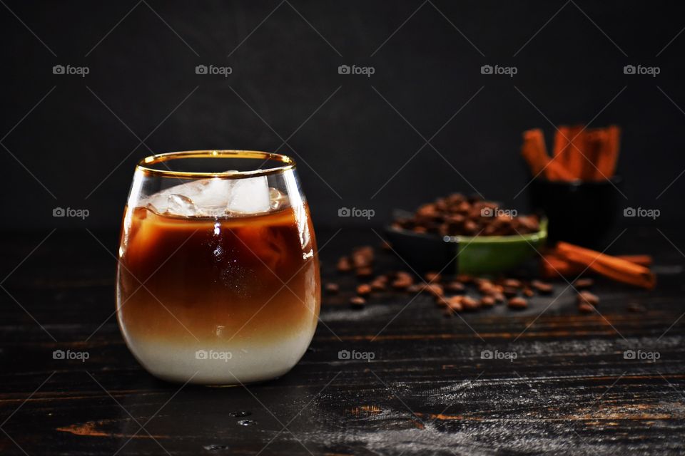 Iced coffee layered over horchata with coffee beans and cinnamon sticks in the background 