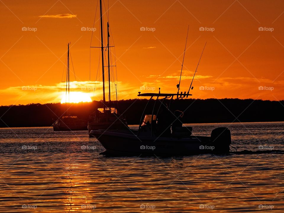 Silhouette of people fishing on sea at sunset