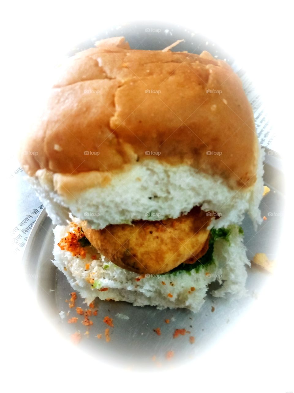 "Vada Pav" The Famous Street Fast Food of Mumbai, India. The dish consists of a deep fried potato dumpling placed inside a bread bun (pav) sliced almost in half through the middle. It is generally accompanied with chutneys and a green chili.