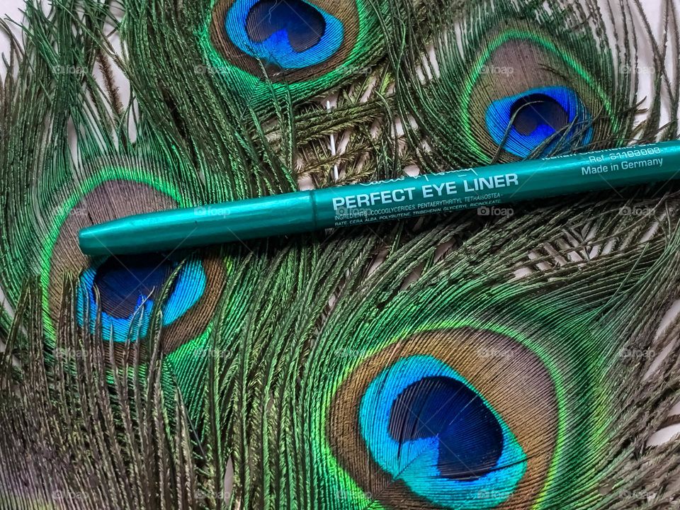 Green eyeliner displayed on a bed on peacock feathers