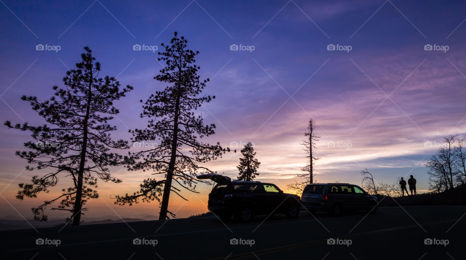 Friends watching a vibrant sunset from the side of a road on a trip. SUV back door open