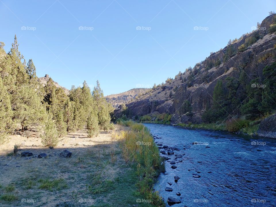 The beautiful Crooked River with fall colored bushes on its banks flows through a canyon formed from andesite and basalt flows on a nice autumn evening in Central Oregon. 