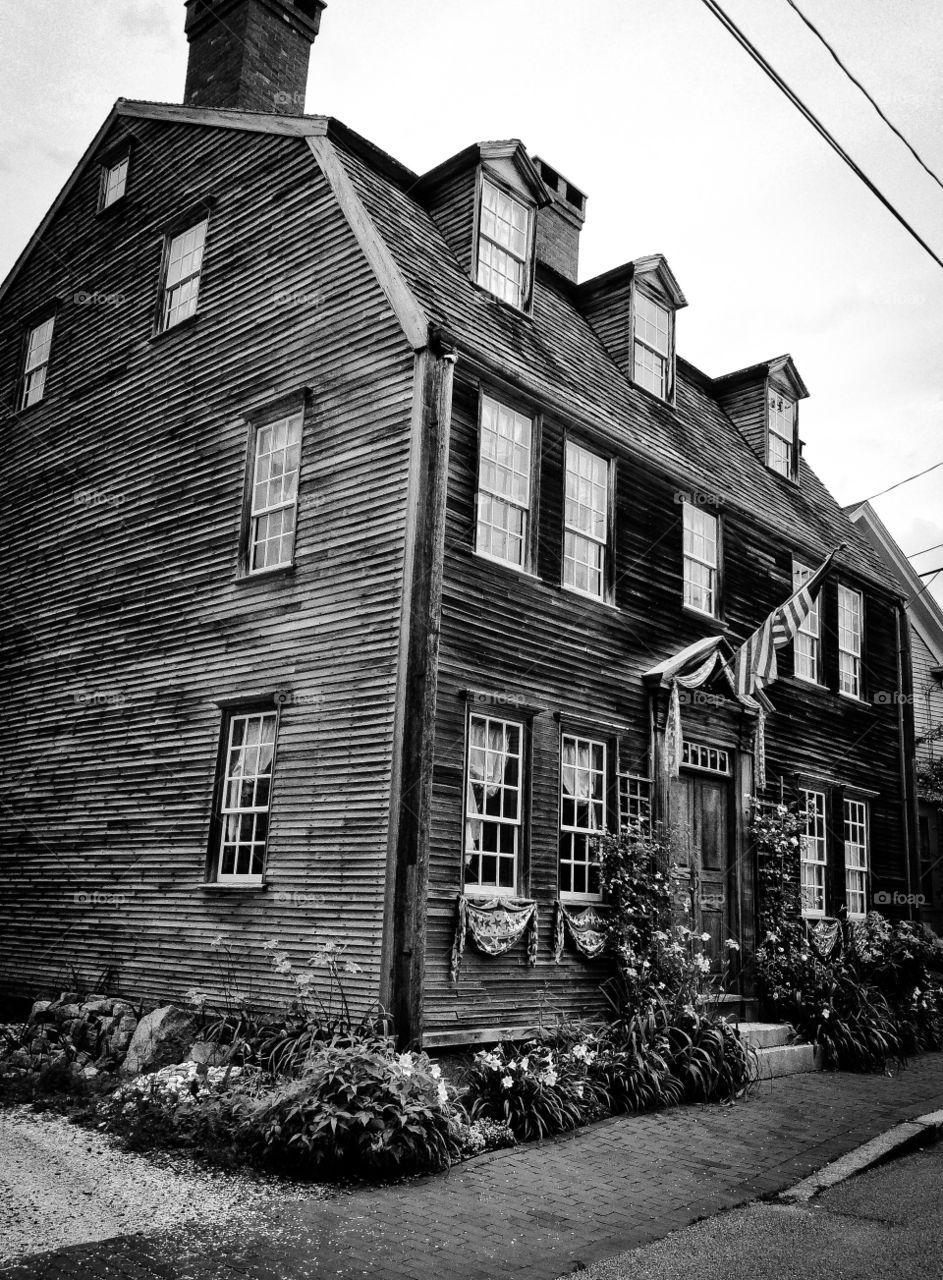B & W historic wooden slat house from the 1700s well kept with flag and flowers