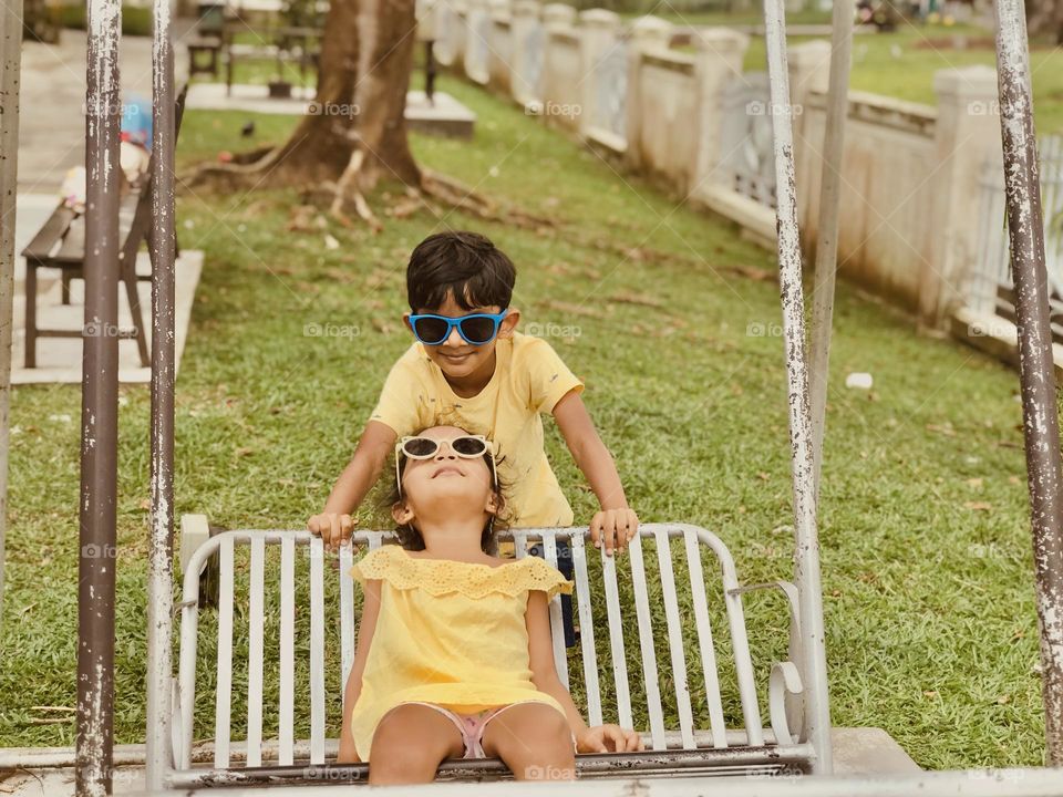 Boy and girl making fun by swinging and brother swings his sister and they both wear yellow dress