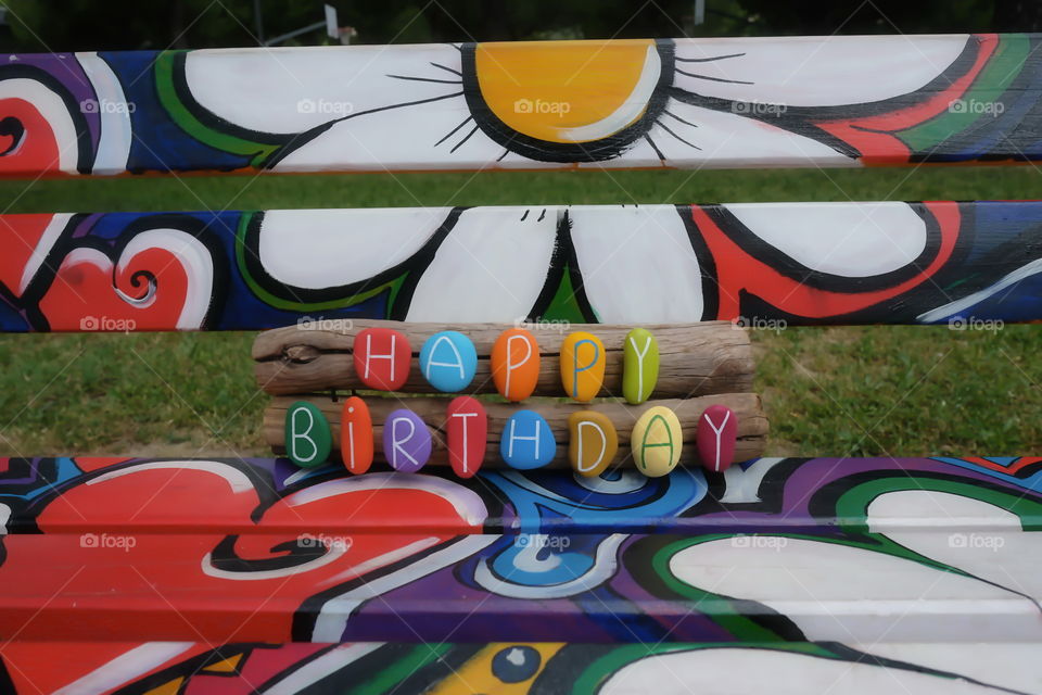 Happy Birthday text with colored stones on a creative painted public bench