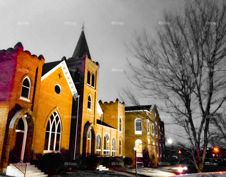 Stunning church in the twilight with a silhouetted tree and bright lights shining upon it. 