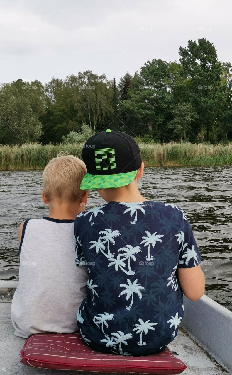 Two boys sitting familiar together at the back of a rowing boat looking on the water