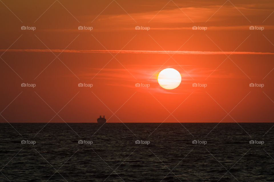 a steamer sailing across the sea leaving the horizon against the backdrop of a huge sunset