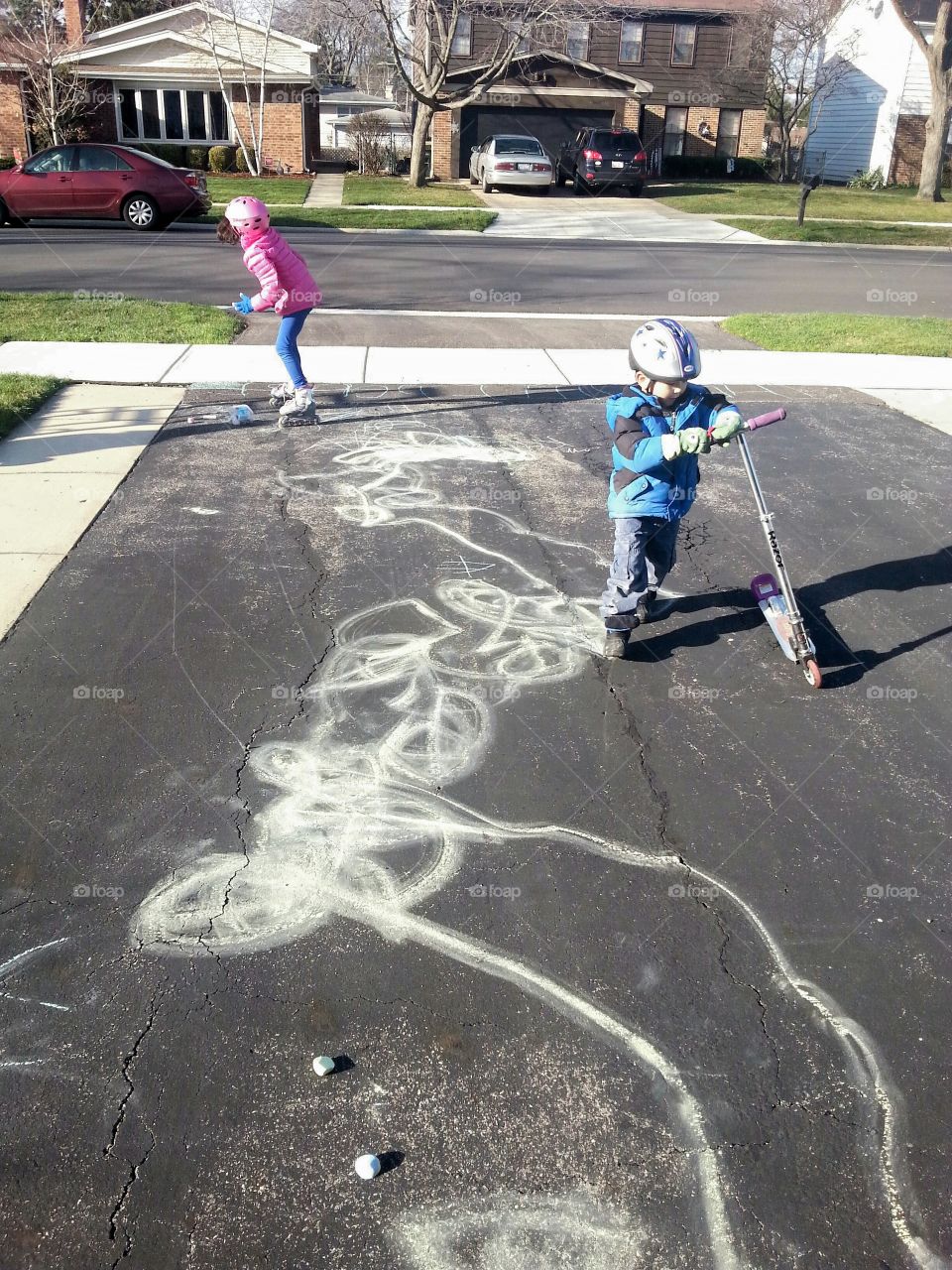 children drawing with chalk using scooter and skates