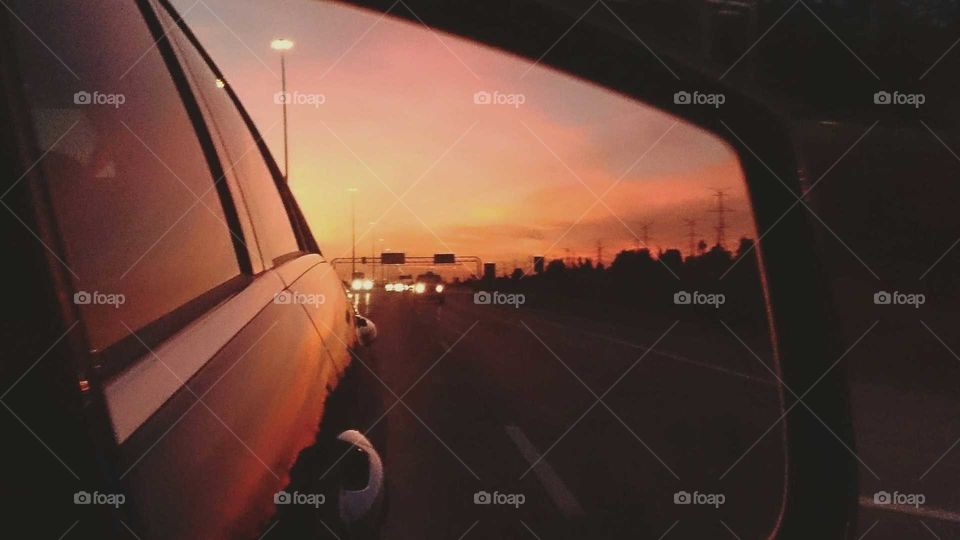 A road view and beautiful sunset caught in a car mirror