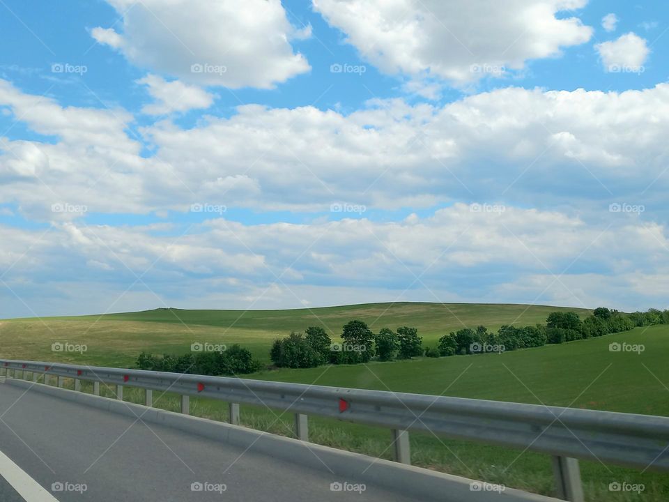 green spaces and blue sky with clouds.