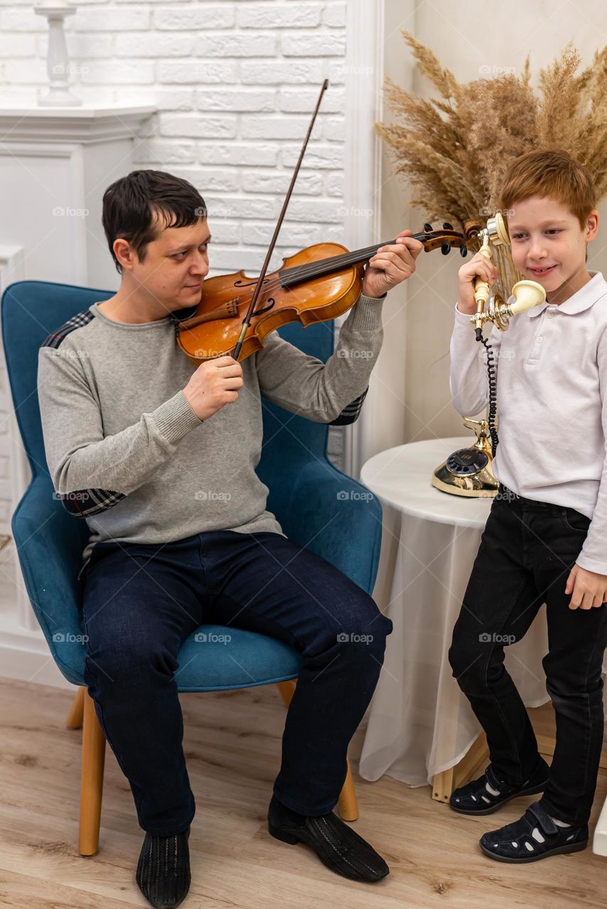 a young man plays the violin in a bright room, his son listens to music