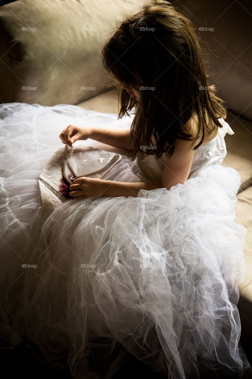 Little girl playing dress up in mom's wedding dress with beautiful natural window light