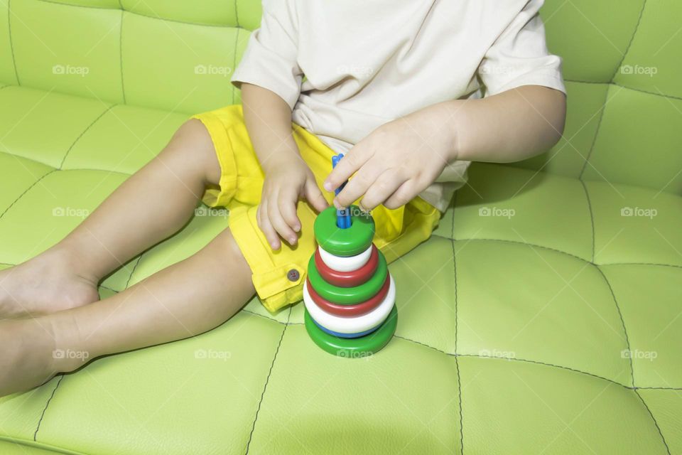 The child is having fun playing a bright pyramid educational toy, sitting on a green sofa.