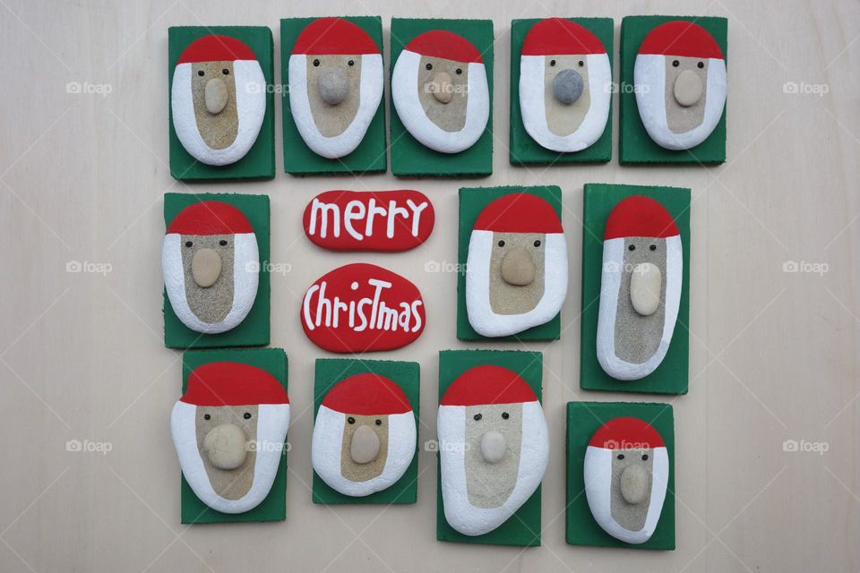 Merry Christmas message composed with handmade Santa Claus heads with colored stones and pebbles on a wooden board