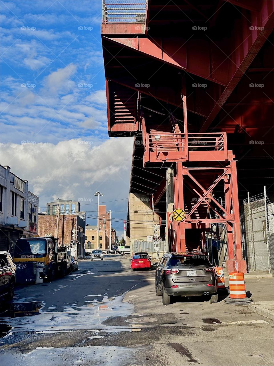 This is the red metal staircase of the “Pulaski Bridge” at “Newtown Creek” in LIC, Queens with its intricate cubist and angular structures seen from the parking lot beneath it. 2023. Hypnotic Productions