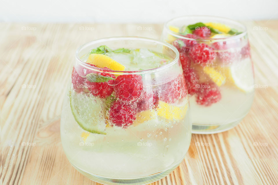 two steaming glasses of ice-cold lemonade made from lemons, lime, mint, and raspberries. the bubbles of soda.