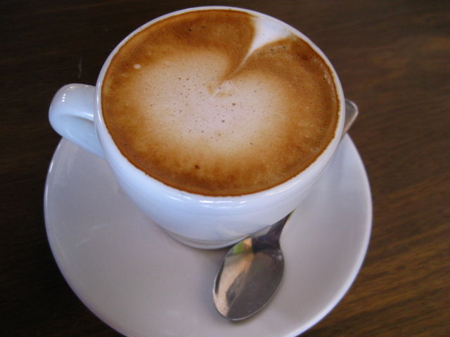 Cappuccino . A cup of cappuccino on a saucer with a spoon. Taken in Oakland, California.