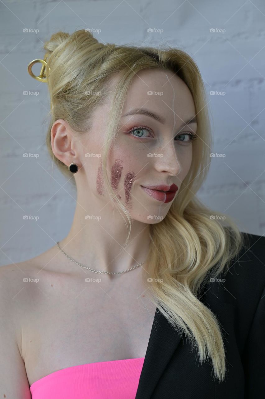 Close-up portrait of a blonde smiling girl with different make-up on half of her face on white background