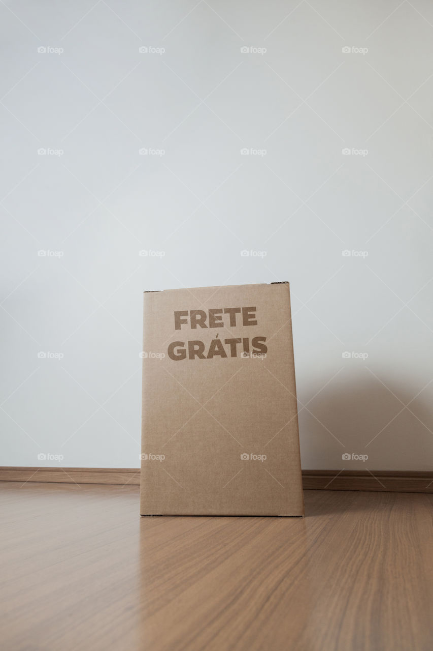 Detail of man with black gloves holding a cardboard box written free shipping to deliver products on gray background. Delivery concept. Delivery service concept. Copy space. Black friday concept.